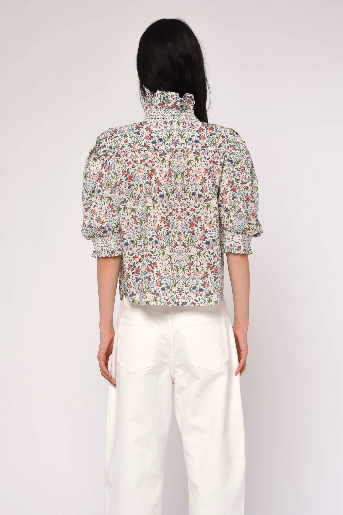 Person wearing a floral blouse and white pants on a plain background