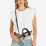 A woman modeling a white sleeveless top and light-wash jeans, wearing a black studded shoulder bag with a long strap and a brown belt.