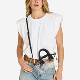 A woman modeling a white sleeveless top and light-wash jeans, wearing a black studded shoulder bag with a long strap and a brown belt.