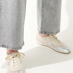 White sneakers with gold accents worn with light gray jeans on a white background