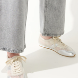 White sneakers with gold accents worn with light gray jeans on a white background