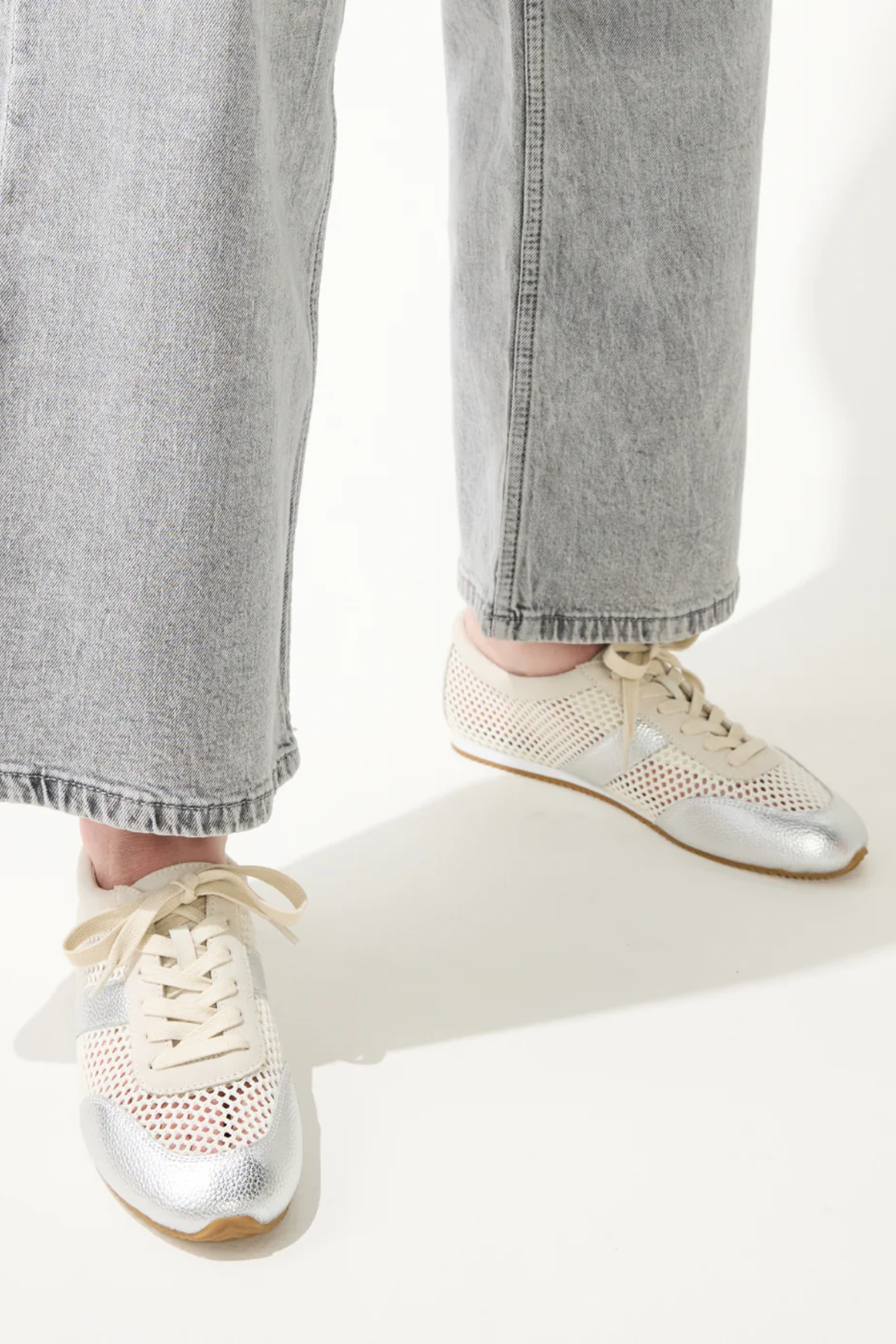 White sneakers with gold accents worn with light gray jeans on a white background