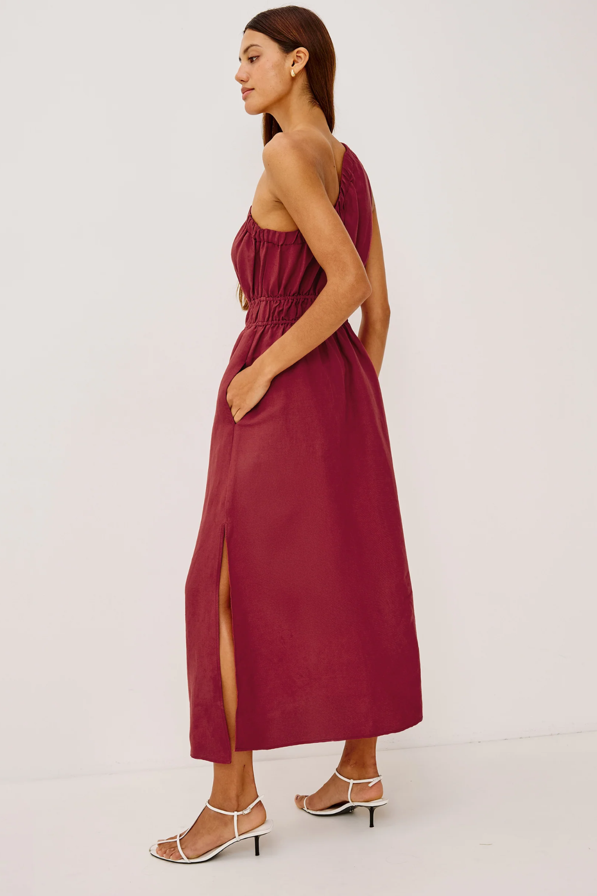 Woman wearing a burgundy strapless dress with a slit on a white background