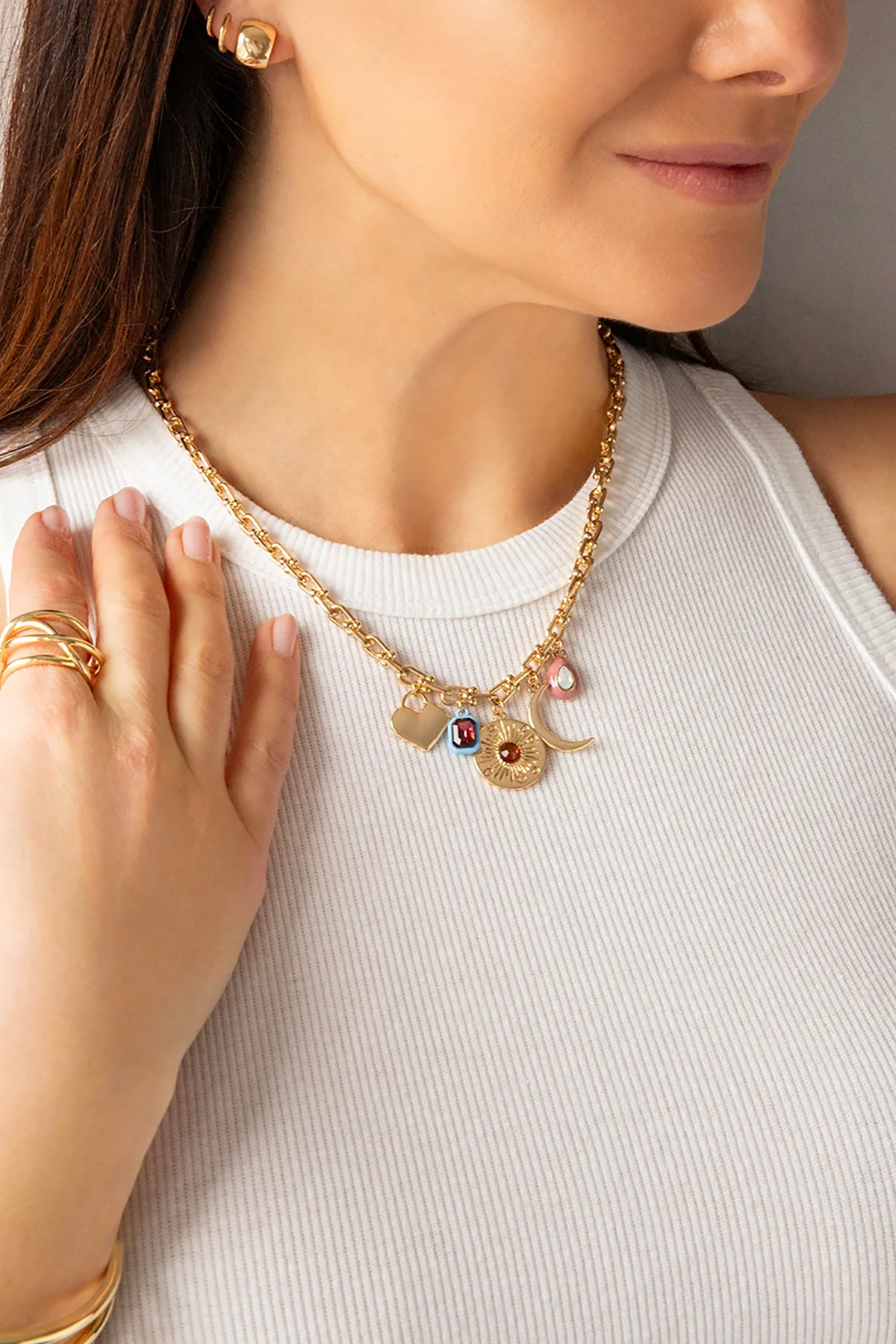 Woman wearing a gold necklace with charms, close-up of neck and hand.