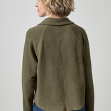 Person wearing a green jacket and blue jeans on a plain background