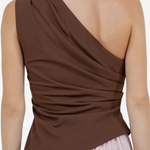 A woman shown from the back wearing a brown draped one-shoulder top and a light pink polka dot skirt against a plain light background.