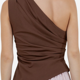 A woman shown from the back wearing a brown draped one-shoulder top and a light pink polka dot skirt against a plain light background.