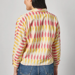 Person wearing a colorful patterned shirt and blue jeans on a gray background