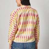 Person wearing a colorful patterned shirt and blue jeans on a gray background