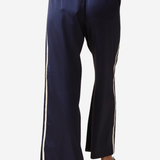 A person wearing navy wide-leg pants with white side stripes, shown from the back against a light gray studio background.