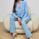 Woman in a blue suit sitting on a beige chair against a plain background