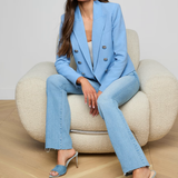 Woman in a blue suit sitting on a beige chair against a plain background