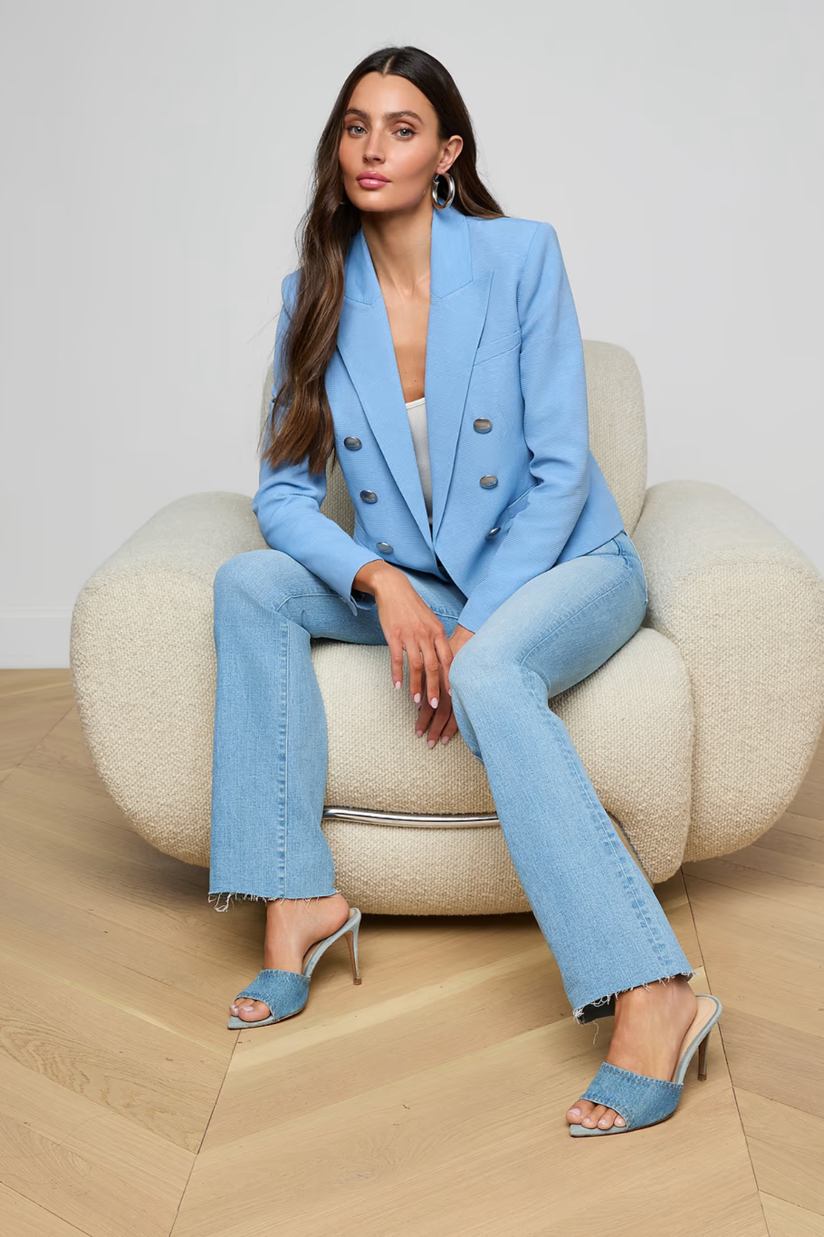 Woman in a blue suit sitting on a beige chair against a plain background