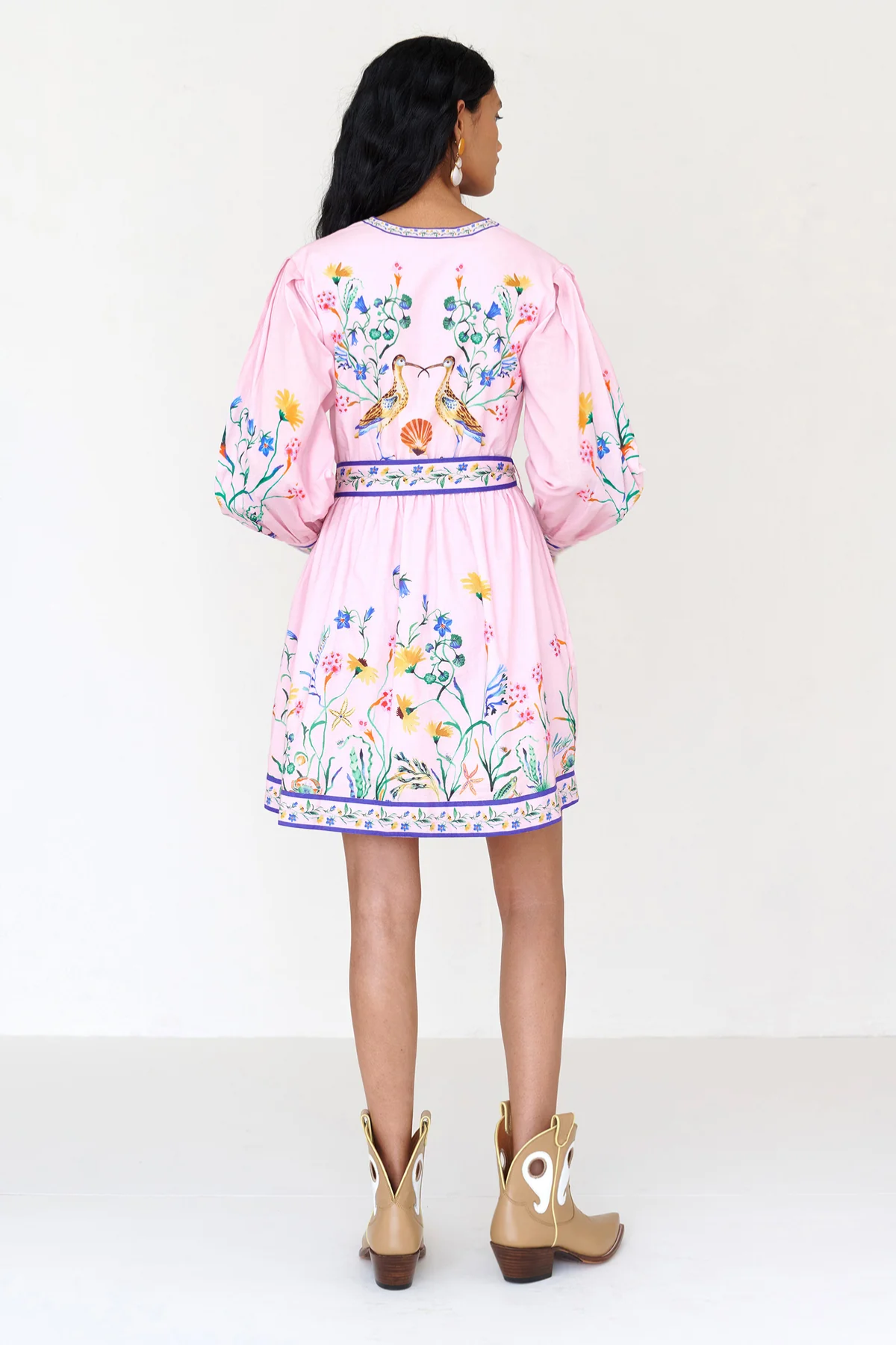 Woman wearing a pink dress with floral embroidery on a white background