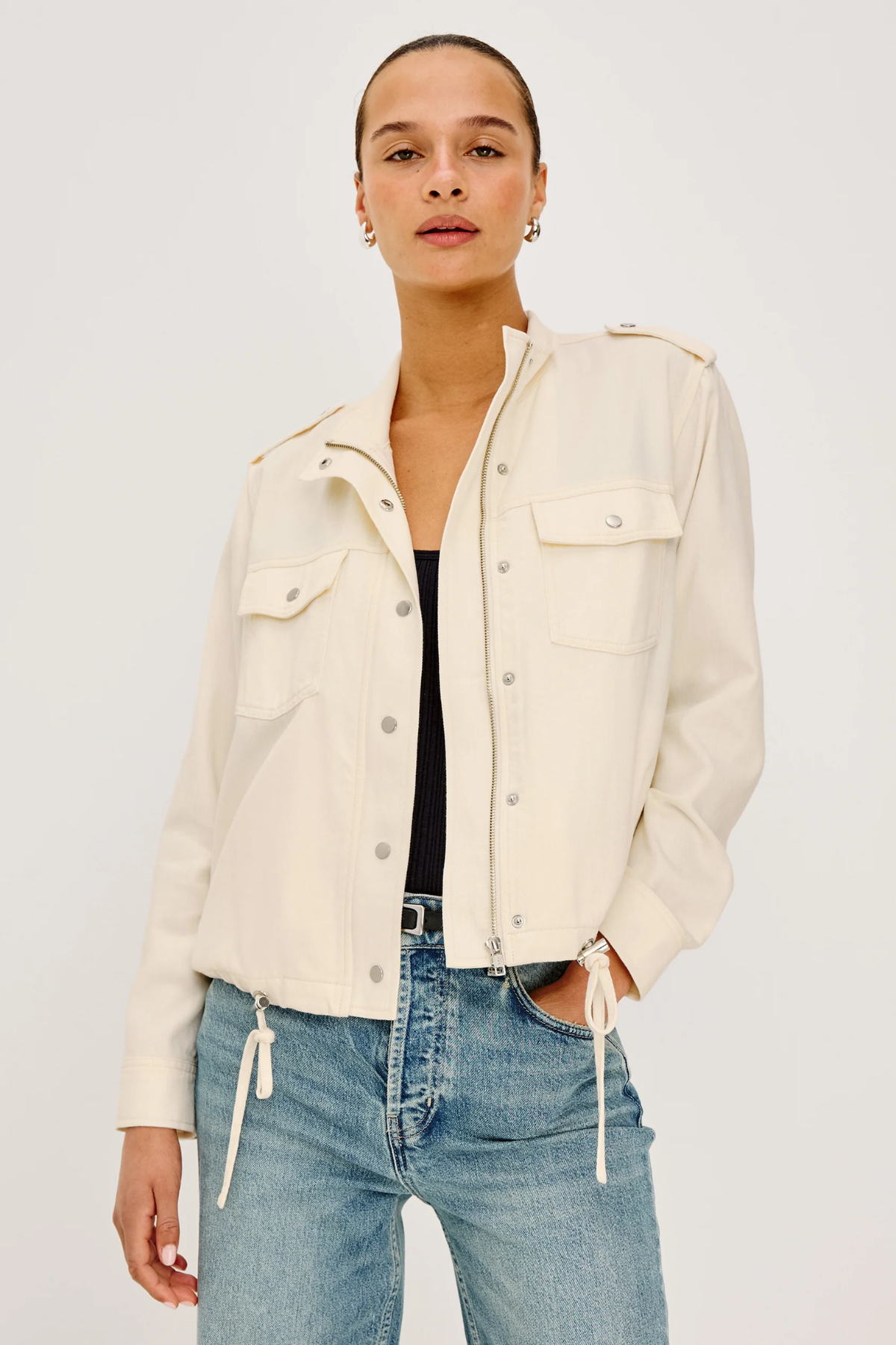 Woman wearing a cream jacket and blue jeans on a white background