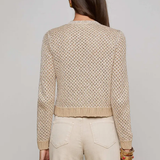 Woman wearing a beige knitted sweater and pants against a plain background