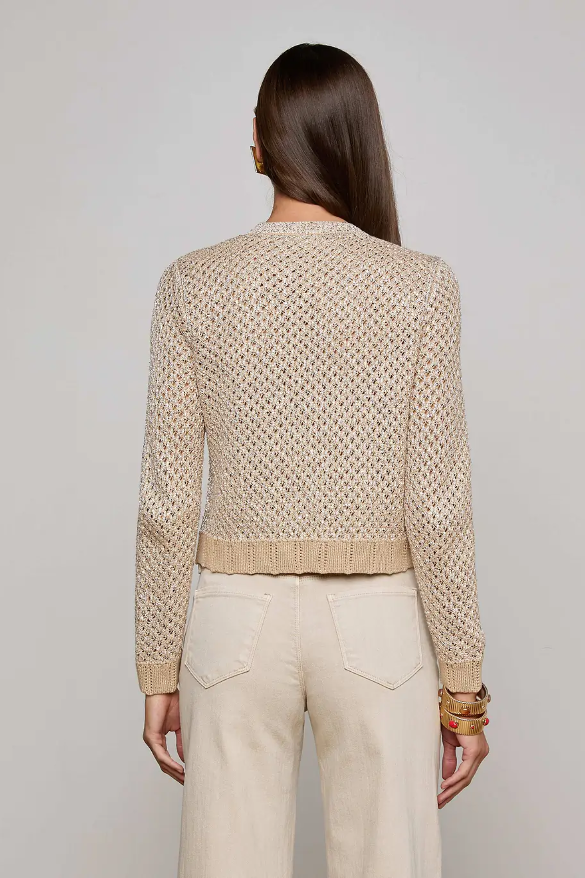Woman wearing a beige knitted sweater and pants against a plain background