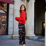 Woman in a red sweater and patterned pants standing in an urban setting.