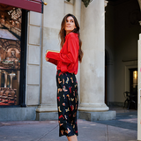 Woman in a red sweater and patterned pants standing in an urban setting.