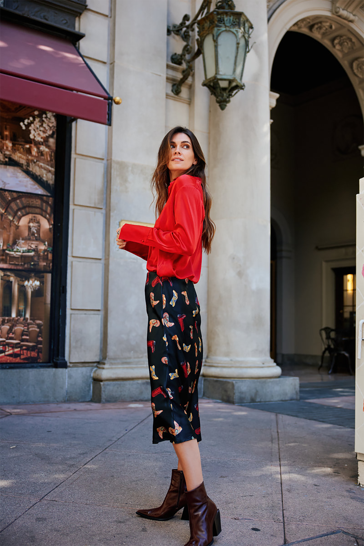 Woman in a red sweater and patterned pants standing in an urban setting.