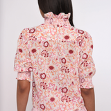 pink printed short sleeve blouse with ruffles on model against a white background