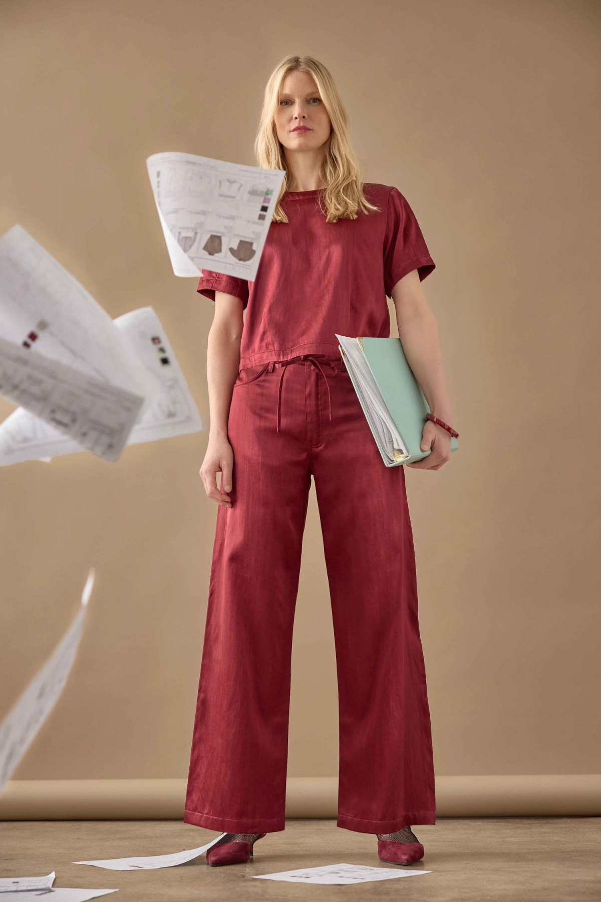 Woman in red outfit holding papers against a beige background