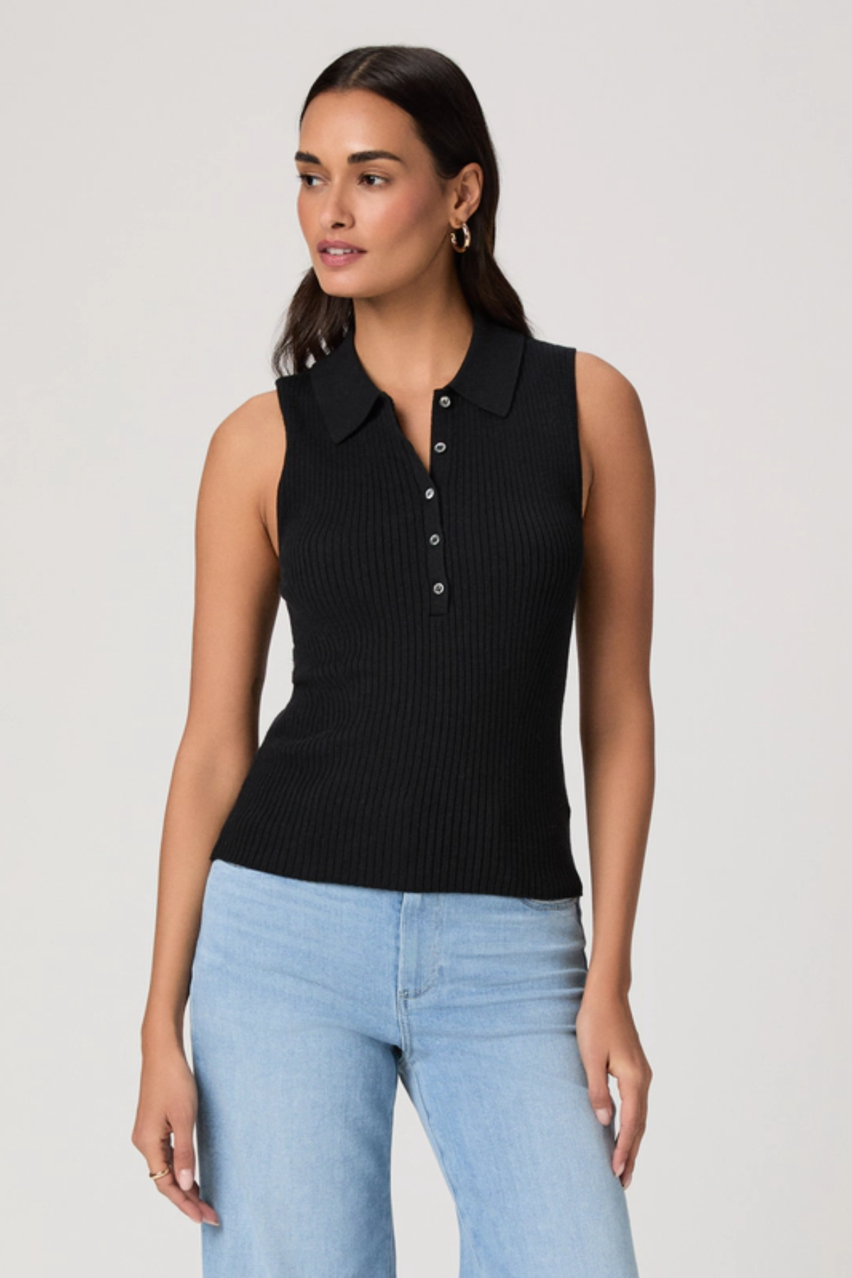Woman wearing a black sleeveless ribbed polo shirt and light blue jeans on a plain background