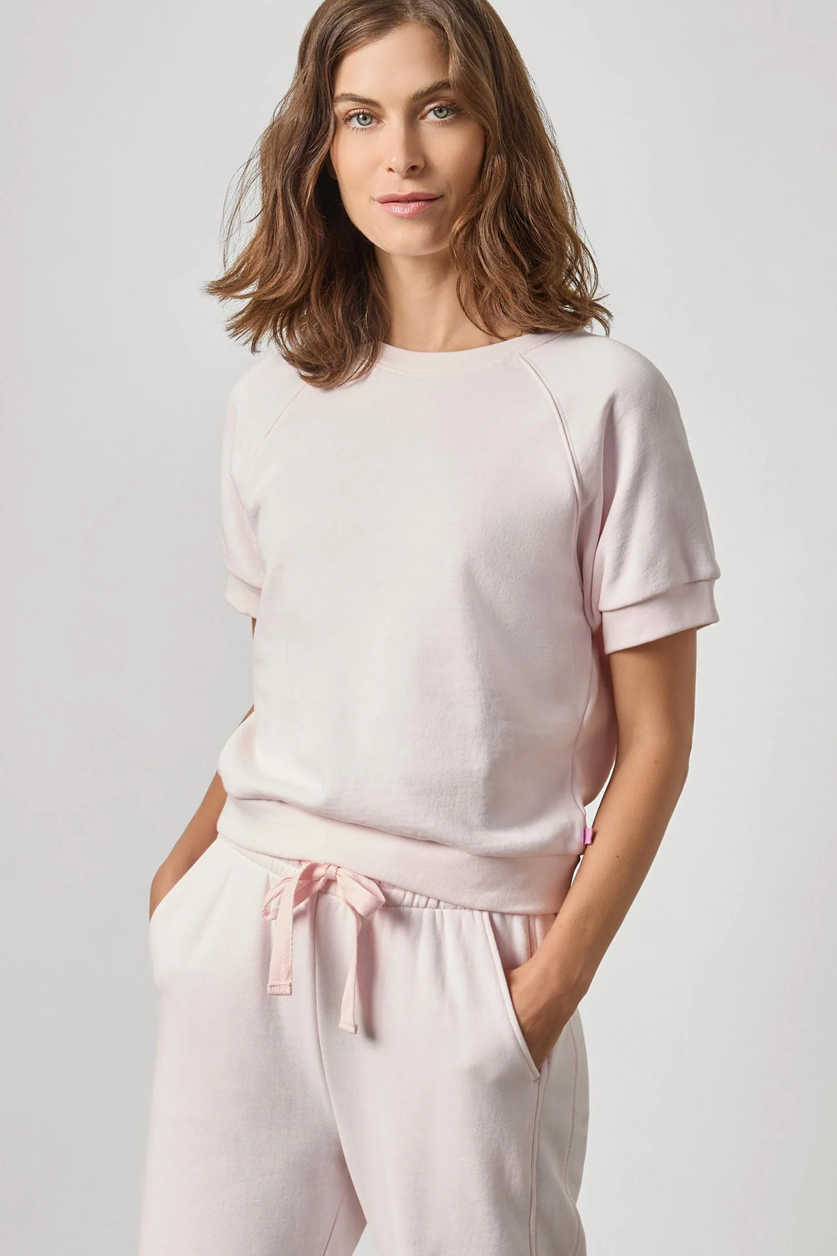 Woman wearing a light pink top and pants on a plain background