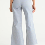 Model wearing light-wash wide-leg cropped denim jeans with rounded flap pockets, welt pocket detailing, and a raw hem, styled with a neutral top against a clean studio background.