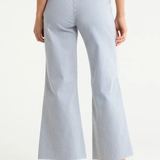 Model wearing light-wash wide-leg cropped denim jeans with rounded flap pockets, welt pocket detailing, and a raw hem, styled with a neutral top against a clean studio background.
