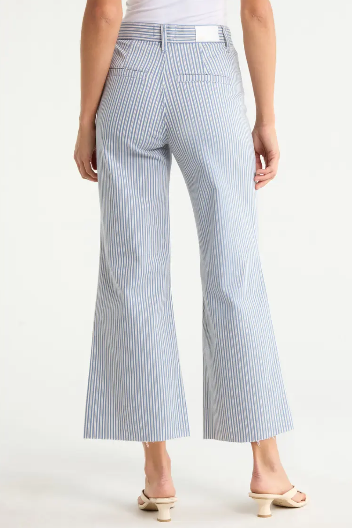 Model wearing light-wash wide-leg cropped denim jeans with rounded flap pockets, welt pocket detailing, and a raw hem, styled with a neutral top against a clean studio background.