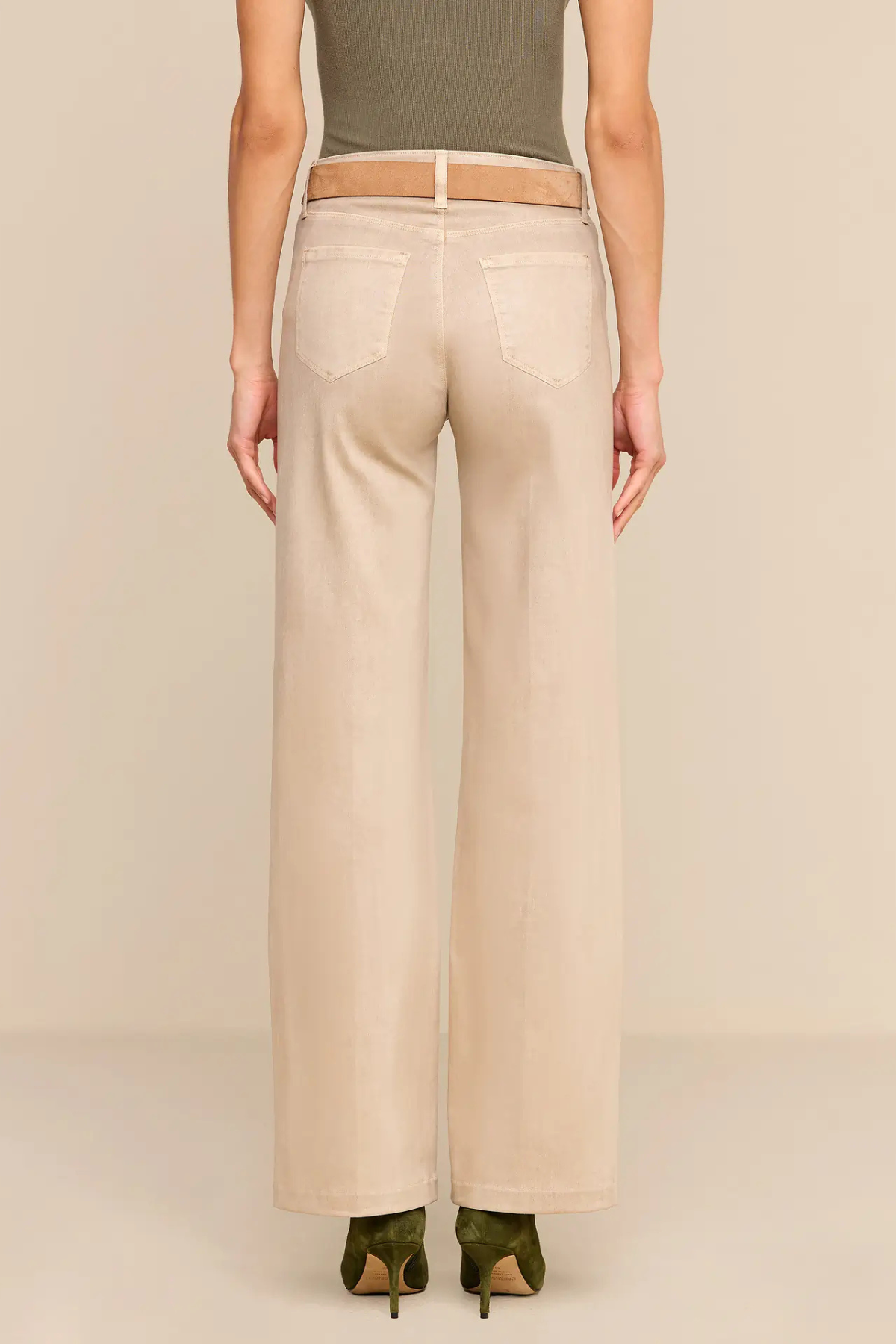 A model shown from the back wearing high-waisted, wide-leg beige pants with a matching beige belt, paired with an olive green top and green pointed-toe heels, set against a solid light beige background.