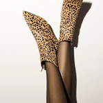 A pair of leopard-print ankle boots worn with sheer black tights, shown against a plain off-white background with a strong shadow.