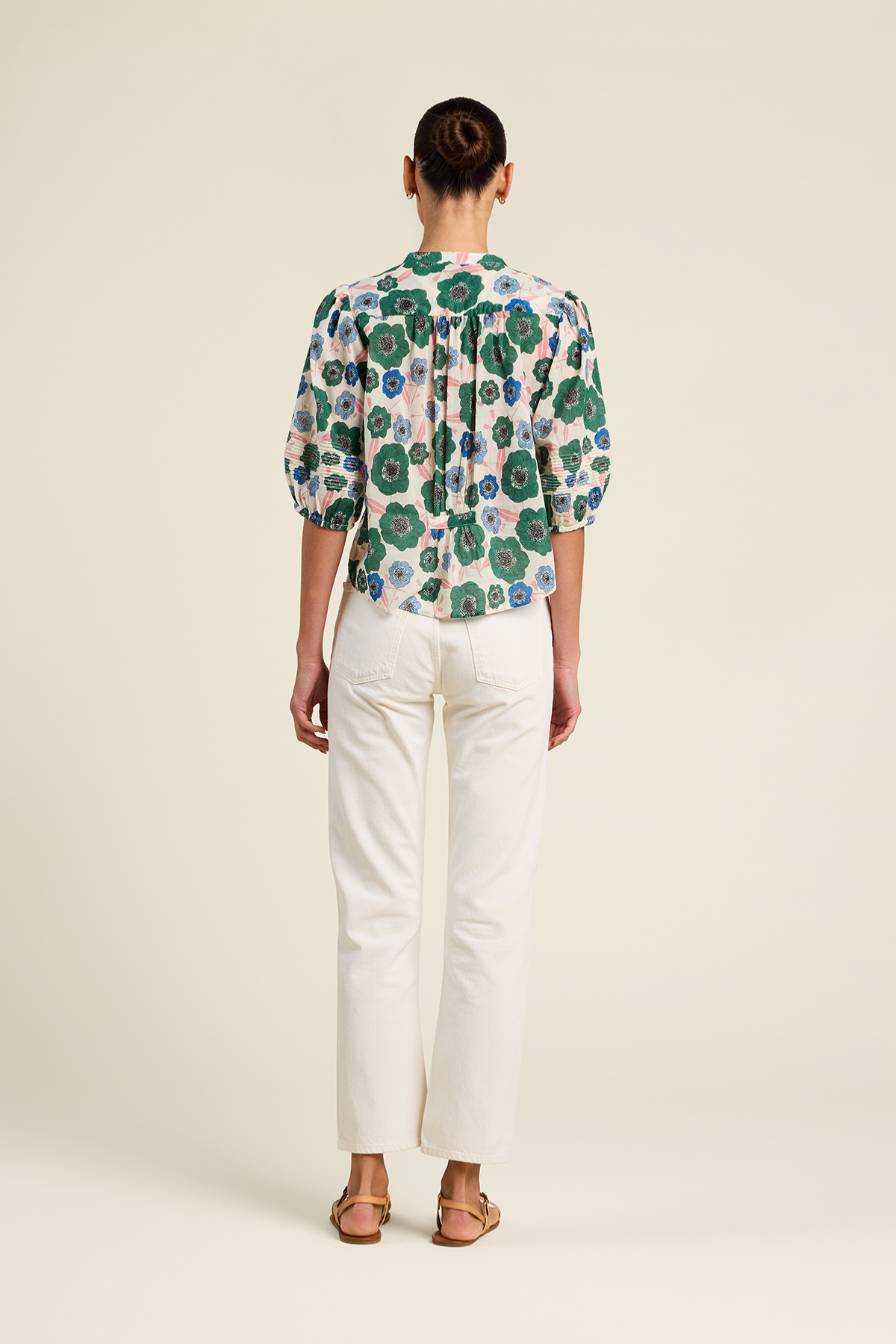 Person wearing a floral blouse and white pants on a plain background