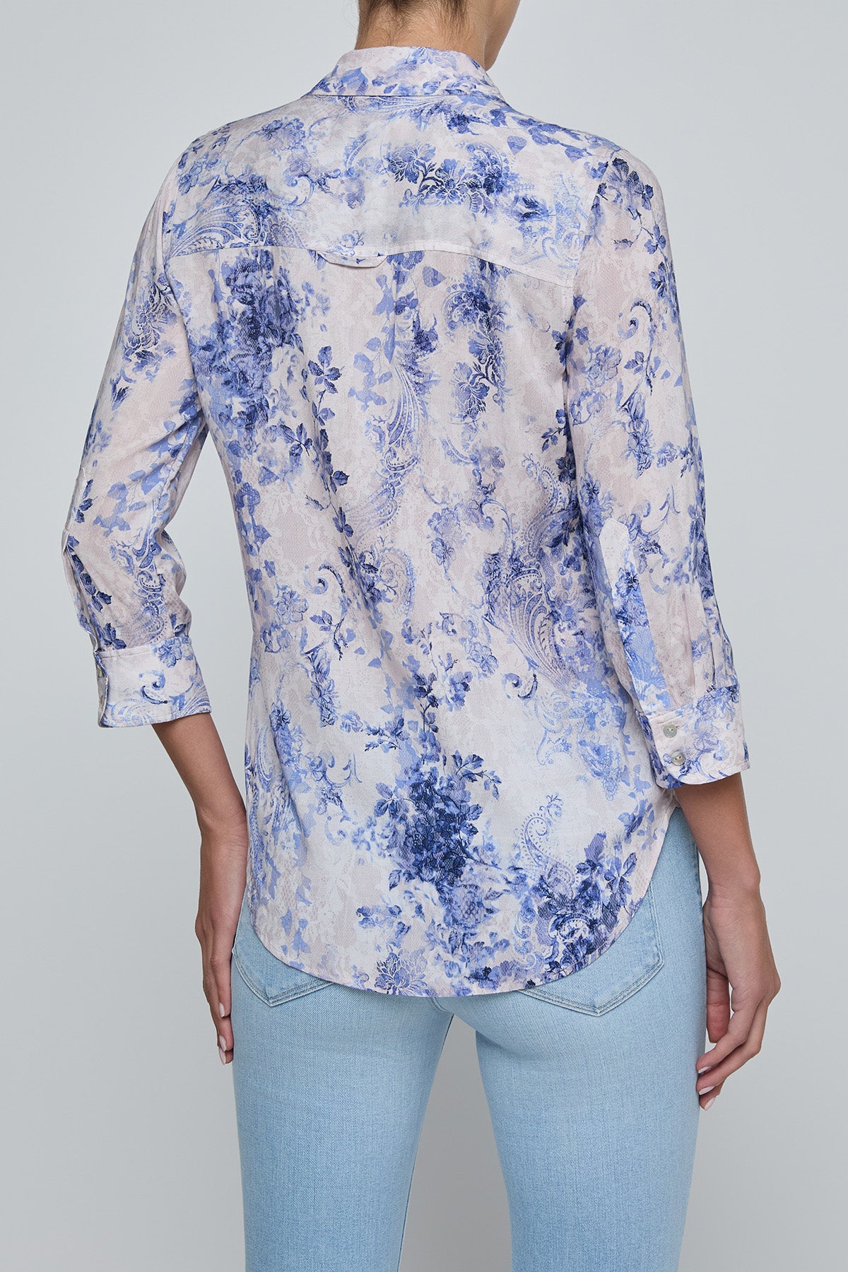 Person wearing a blue floral shirt and light blue jeans on a gray background
