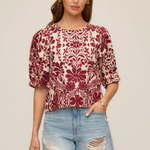 Woman wearing a patterned top and denim shorts on a beige background