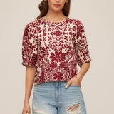 Woman wearing a patterned top and denim shorts on a beige background