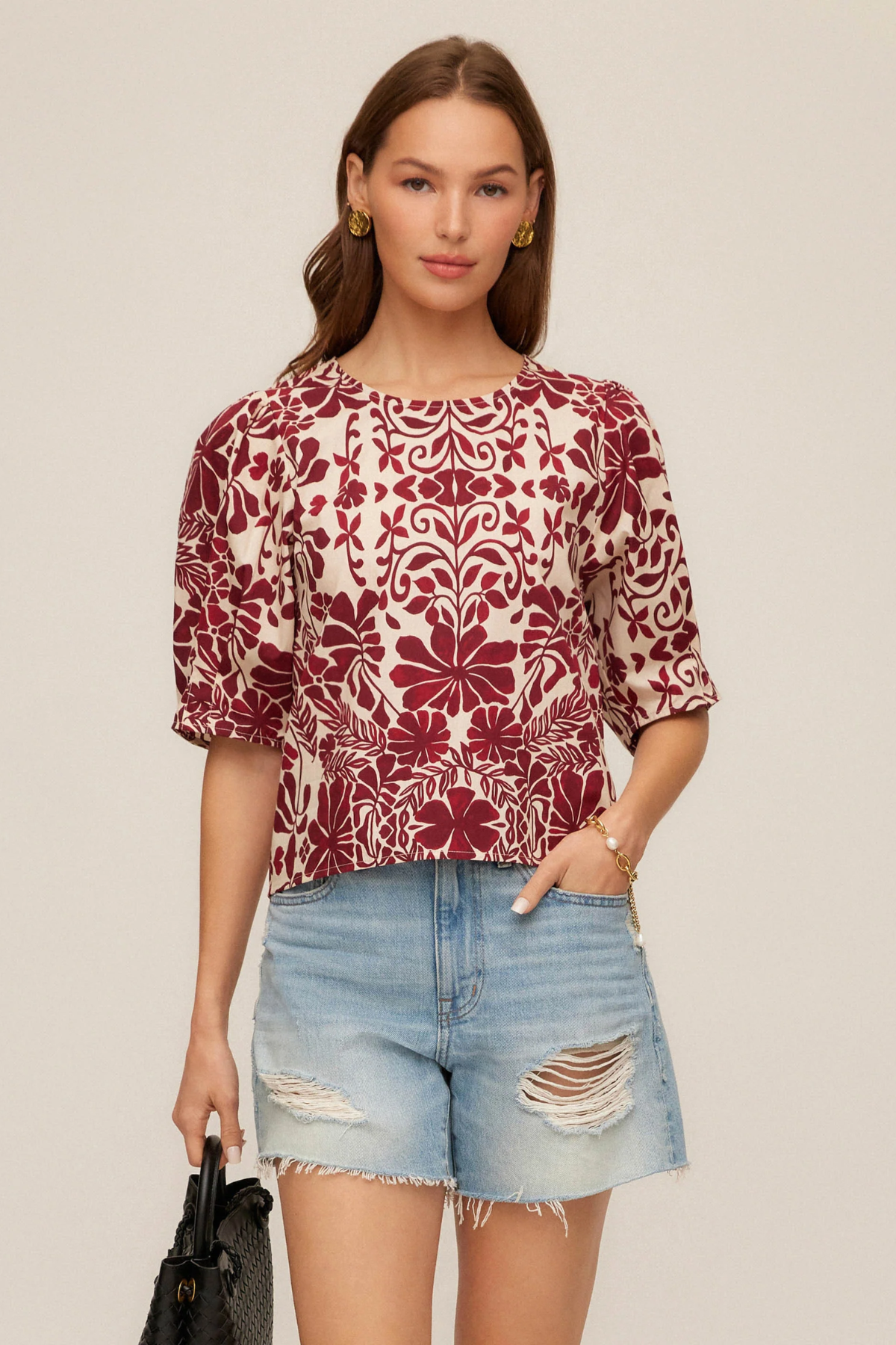 Woman wearing a patterned top and denim shorts on a beige background