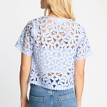 Woman wearing a light blue lace top and jeans on a white background