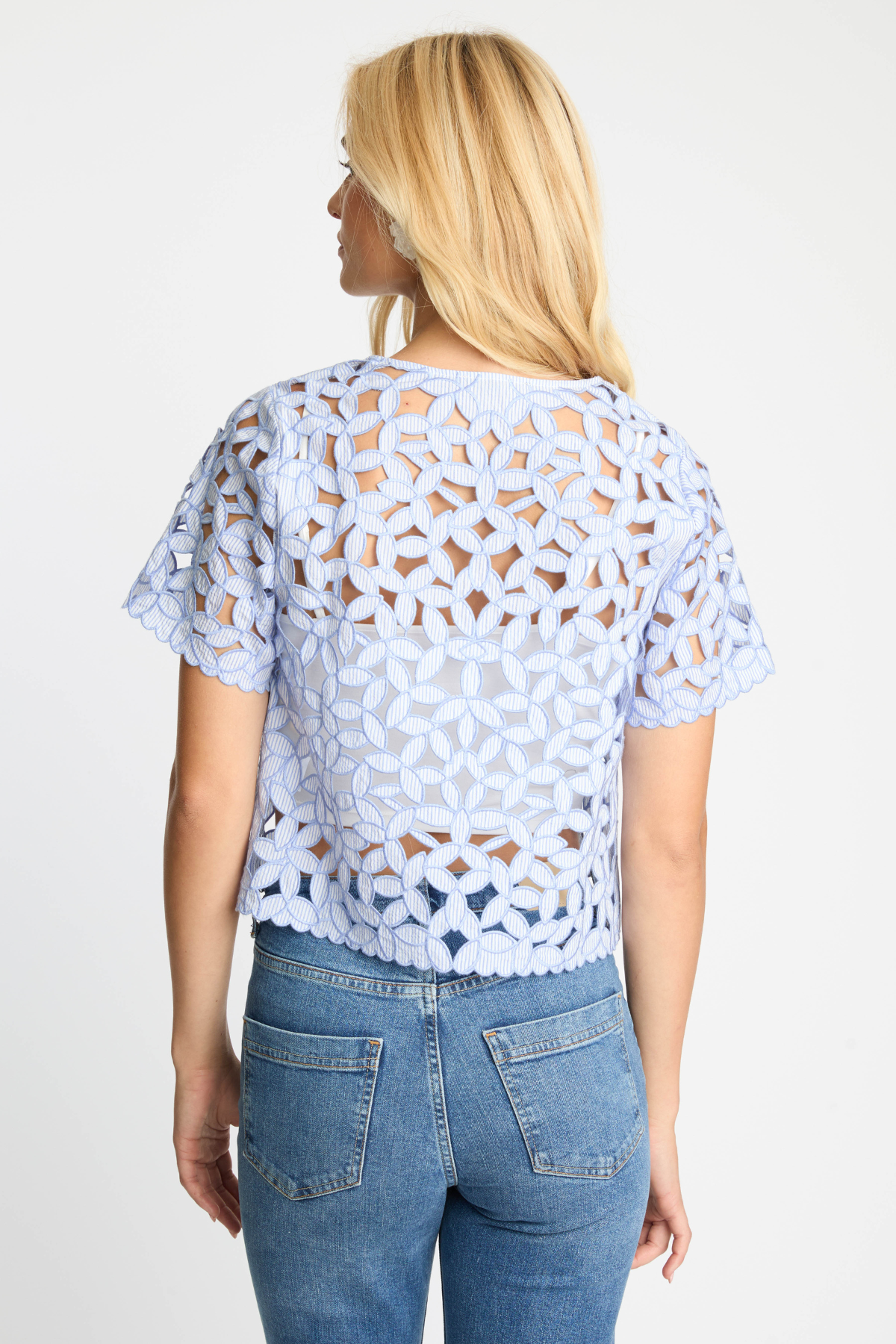 Woman wearing a light blue lace top and jeans on a white background