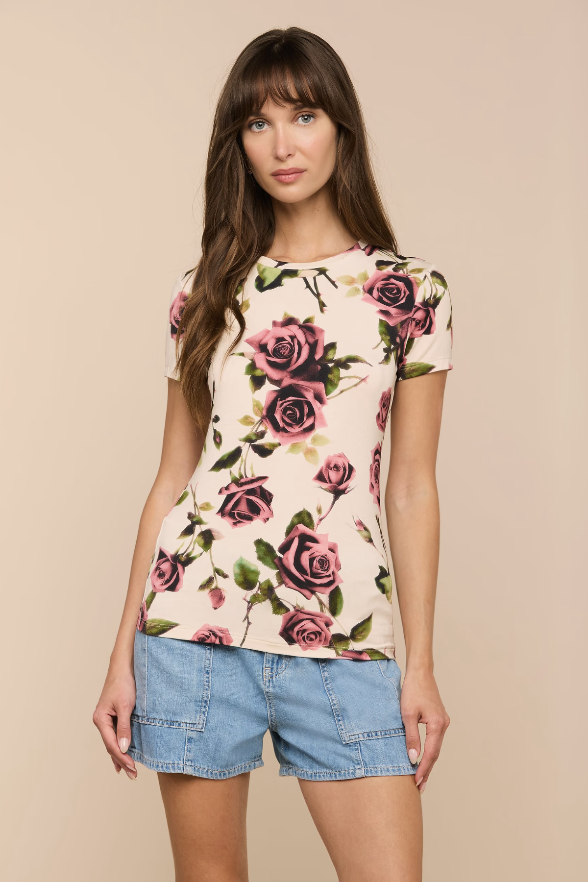 Woman wearing a floral top and denim shorts against a beige background