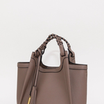 A taupe brown pebbled leather handbag with braided top handles, a tassel detail, and gold hardware, shown on a plain light gray background.