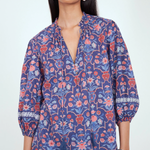 A woman wearing a blue floral print blouse with red and pink floral motifs, paired with light blue jeans, against a plain white studio background.