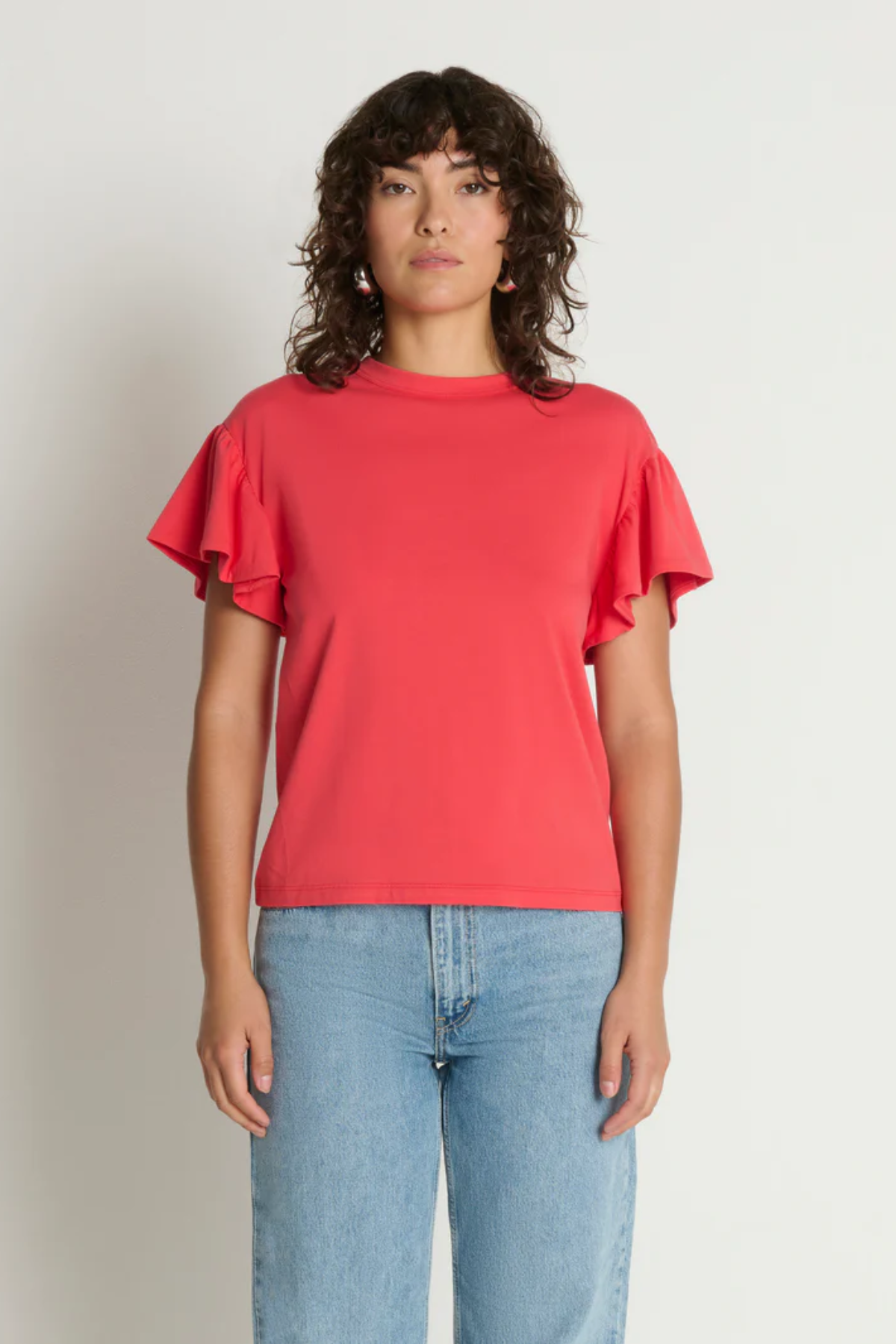 Woman wearing a red ruffled sleeve top and blue jeans against a plain background