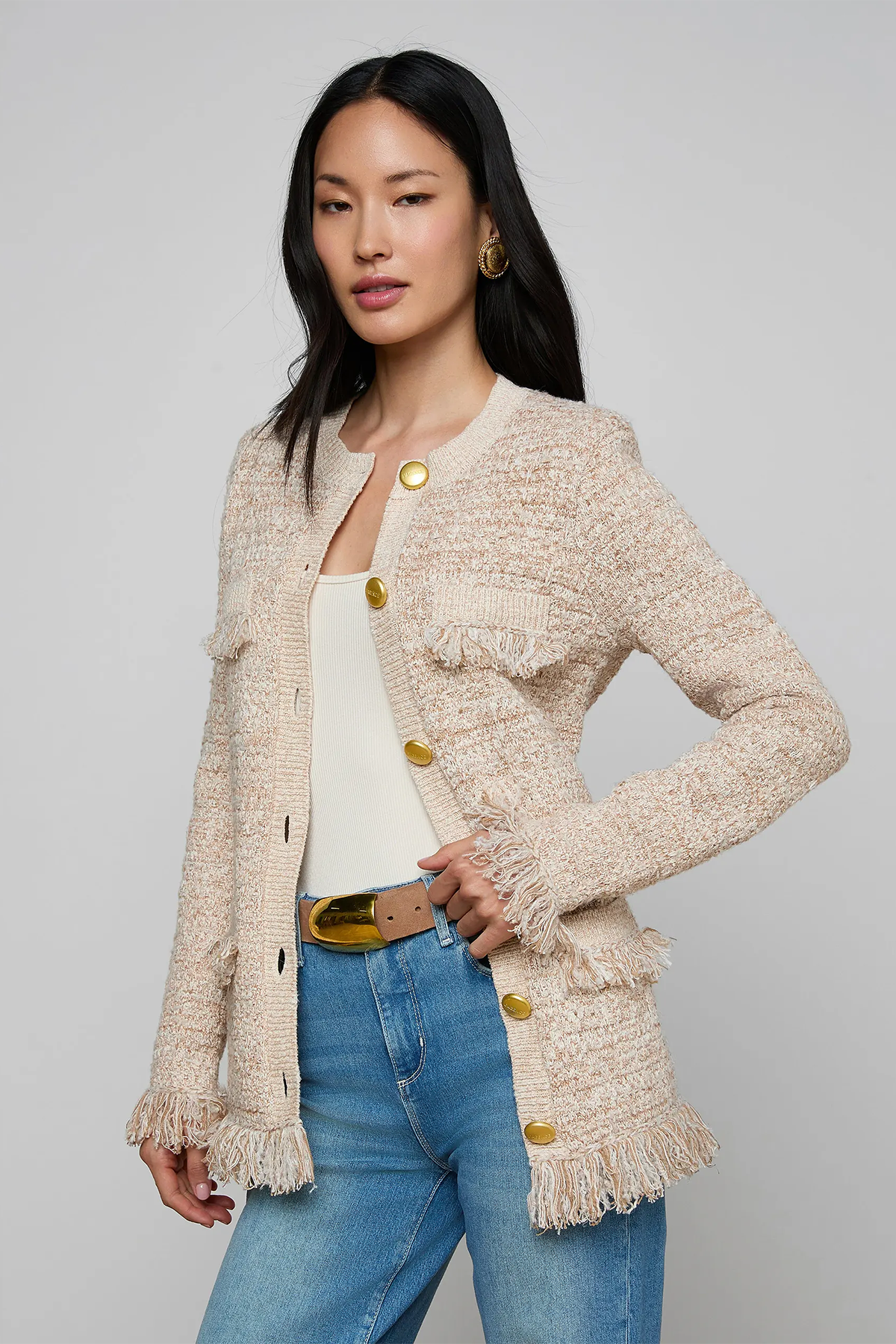 Woman wearing a beige textured cardigan with gold buttons on a gray background