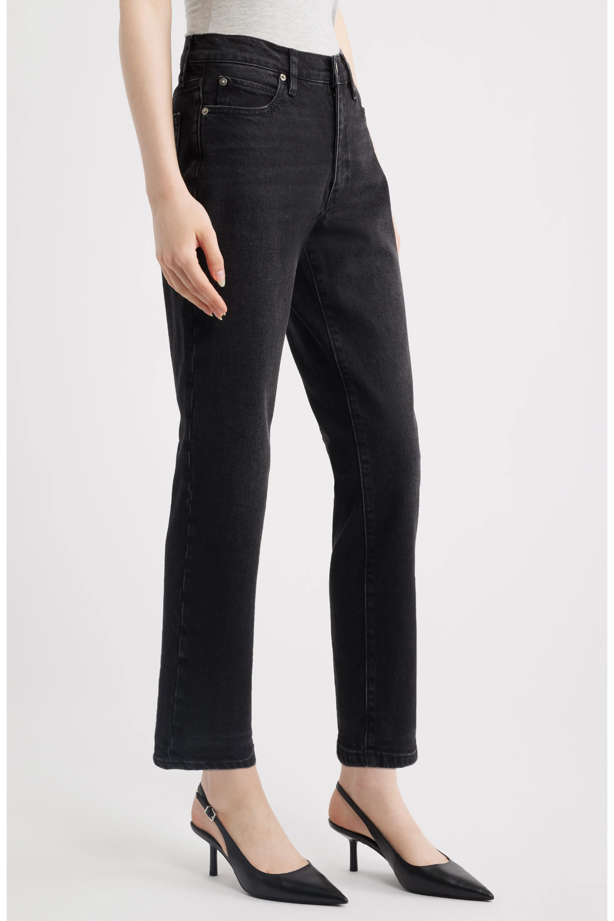 A model wearing black cropped straight-leg jeans with a faded wash, paired with black slingback heels, shown from the waist down on a light gray studio background.