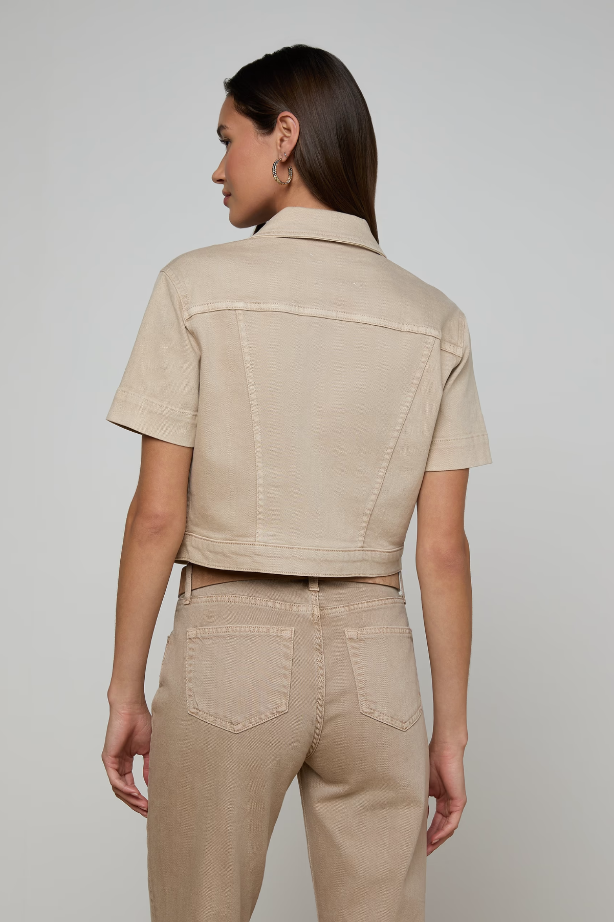 Woman wearing a beige jacket and pants on a plain background