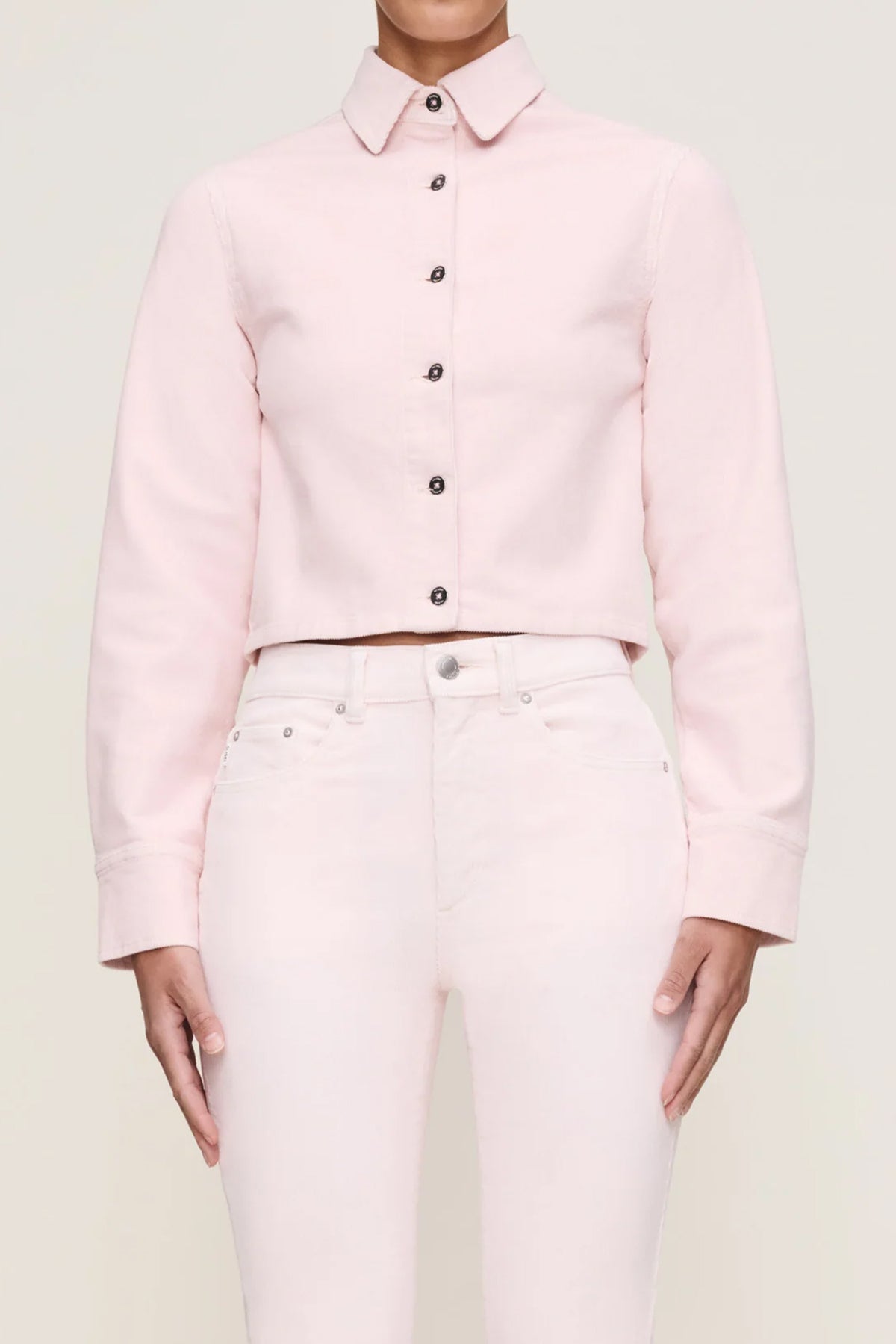 Person wearing a light pink button-up shirt and matching pants on a plain background