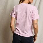 Person wearing a pink t-shirt and dark pants against a plain background