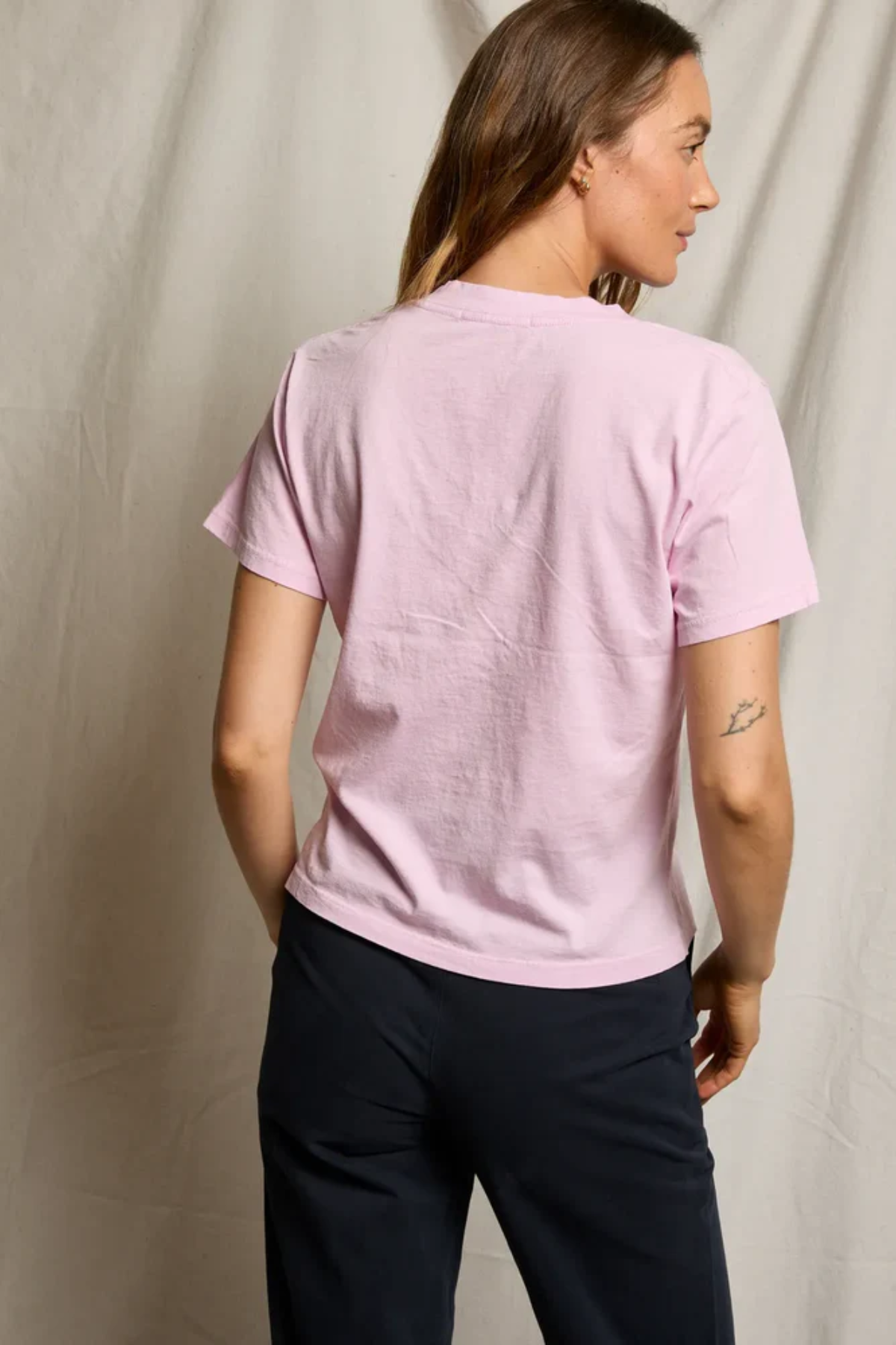 Person wearing a pink t-shirt and dark pants against a plain background